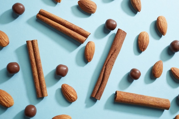 Um padrão criativo feito de paus de canela, amêndoas e bolas de chocolate, as sombras se refletem em um fundo de papel azul