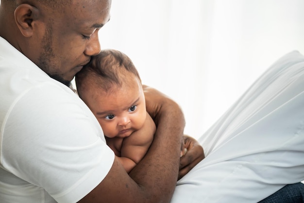 Um pai afro-americano beijando a cabeça de seu filho recém-nascido de 3 meses com felicidade e proteção