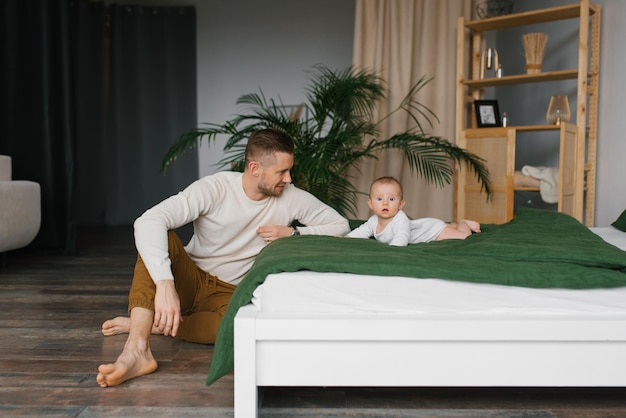 Um pai alegre e feliz está sentado ao lado da cama em que seu filho está deitado e sorrindo