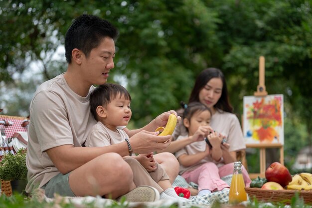 Um pai asiático atencioso descascando suavemente uma banana para seu filho durante um piquenique familiar em um parque público verde