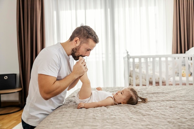 Um pai brincalhão está brincando com sua filhinha e colocando os pés dela na boca em casa