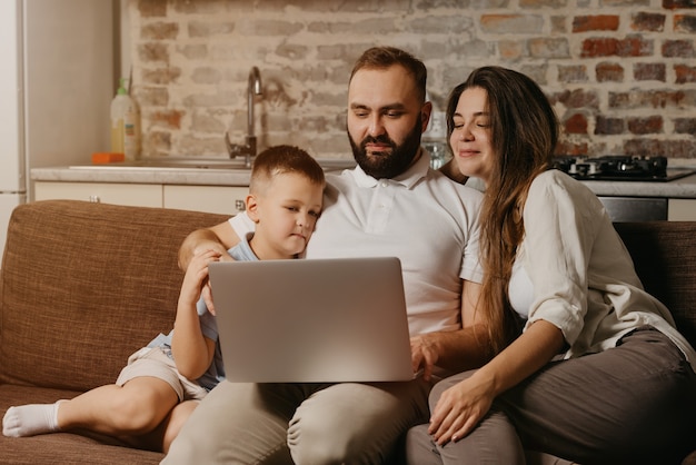 Foto um pai com barba está trabalhando remotamente em um laptop enquanto seu filho e sua esposa feliz estão olhando para a tela