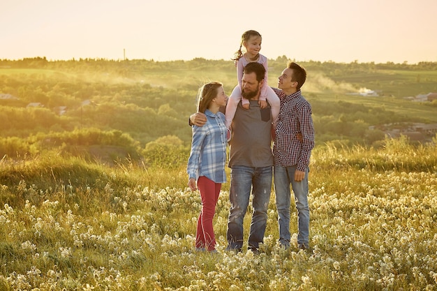 Um pai com três filhos na natureza, um homem abraça suas filhas e filho em um campo ao pôr do sol, dia dos pais