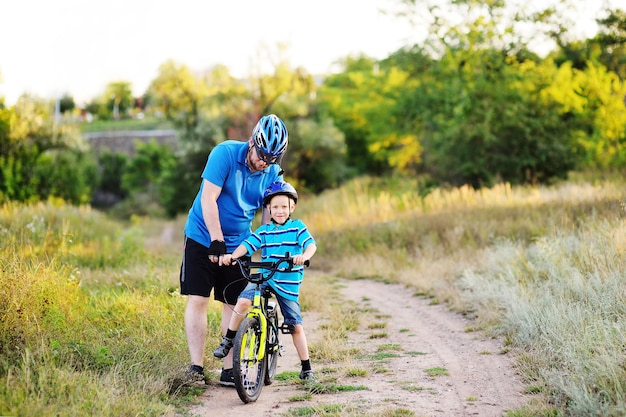 Um pai ensina um filho pequeno de um filho com um capacete protetor a andar de bicicleta