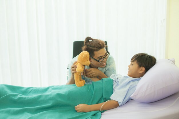 Um pai está segurando a mão dele. e encorajando o filho que está gravemente doente e descansando na cama em um hospital