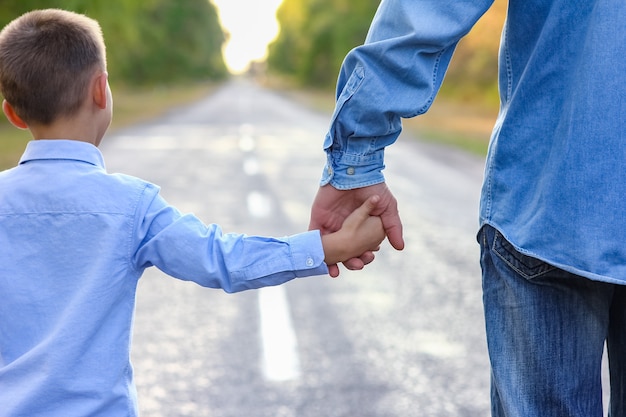 Um pai feliz com uma criança no parque e as mãos na viagem pela natureza vão ao longo da estrada