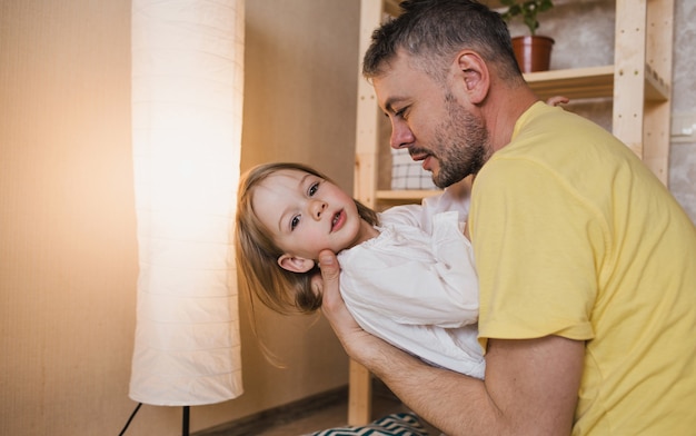 Foto um pai feliz e carinhoso brinca com sua filha, segurando-a nos braços. o conceito de felicidade em casa