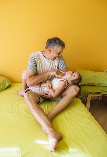 Um pai feliz está brincando na cama com sua filha. diversão e alegria de férias conjuntas