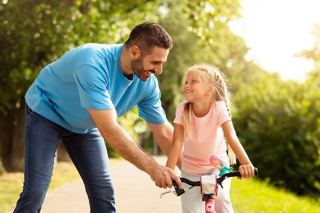 Um pai guia uma menina aprendendo a andar de bicicleta com seu pai no parque se divertindo juntos em