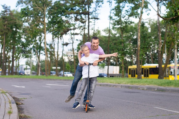 Um pai monta seu filho em uma camiseta branca em uma scooter, a criança feliz espalha as mãos