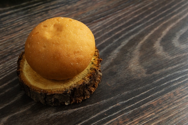 Um pão de hambúrguer encontra-se em um tronco de árvore cortado em uma mesa de madeira.
