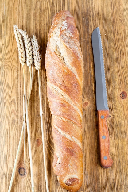 Foto um pão fresco de cor clara com uma crocante deliciosa, close-up na cozinha com uma faca e espigas de coto