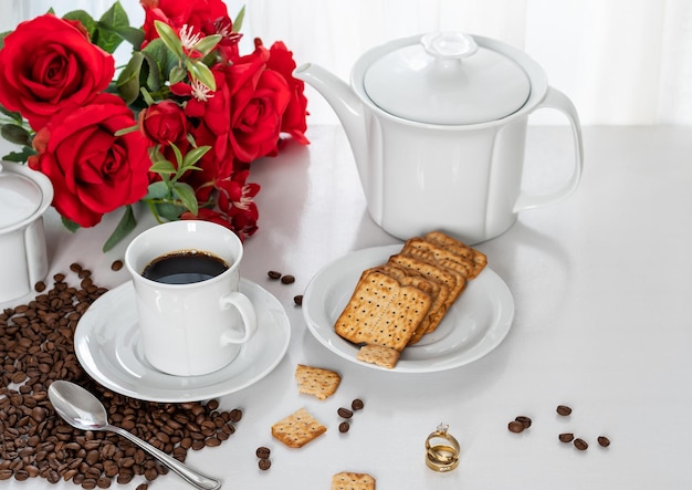 um par de alianças em uma mesa com, xícara com café, biscoitos integrais em um pires