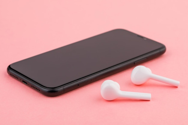 Um par de fones de ouvido brancos e smartphone preto em fundo rosa