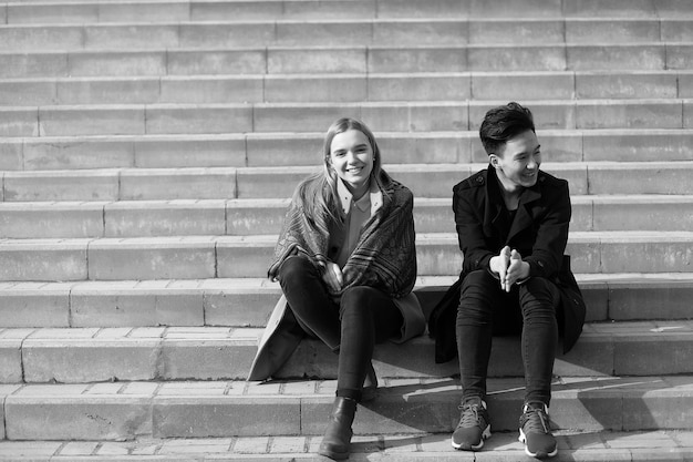 Um par de jovens se conheceram no parque Os amantes estão sentados em um banco no parque de outono da cidade Um menino asiático e uma menina branca sentada em um banco do parque