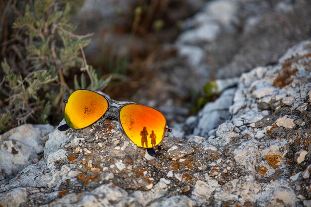 Um par de óculos de sol banhados em luz laranja em uma pedra do mar com o reflexo de turistas neles