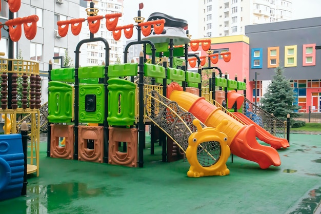 Um pátio de prédios altos com um novo e moderno playground colorido e grande em um dia chuvoso de verão sem pessoas. Parque infantil vazio ao ar livre. Um espaço para jogos e esportes infantis.