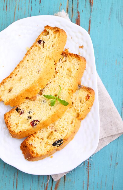 Um pedaço de bolo com passas e frutas cristalizadas em um prato branco sobre um fundo azul