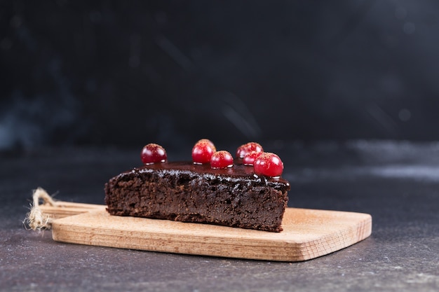 Um pedaço de bolo de chocolate sem glúten decorado com cranberries na placa da cozinha, sobre um fundo preto desfocado. Alimentação saudável.