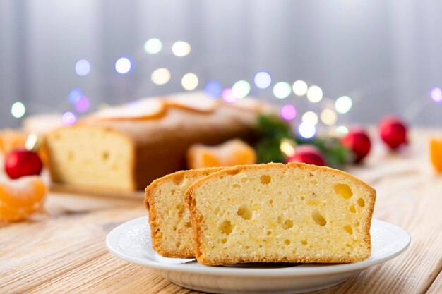 Foto um pedaço de bolo de cítricos em um prato em uma tábua de madeira rústica com tangerinas cheias e decorações de natal no fundo receita fácil de bolo para cozinhar todos os dias feliz natal e feliz ano novo