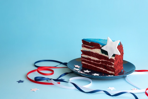 Um pedaço de bolo em forma de bandeira dos EUA com fitas brancas, vermelhas e azuis e estrelas sobre um fundo azul, comemorando o dia da independência, close-up.