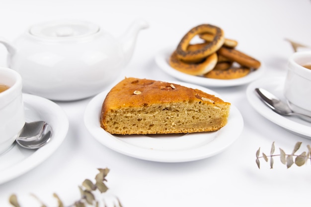 Um pedaço de bolo em um pires com uma xícara de chá ou café e uma chaleira