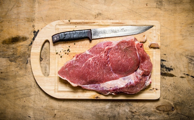 Um pedaço de carne crua com faca na placa de madeira. em uma mesa de madeira. vista do topo