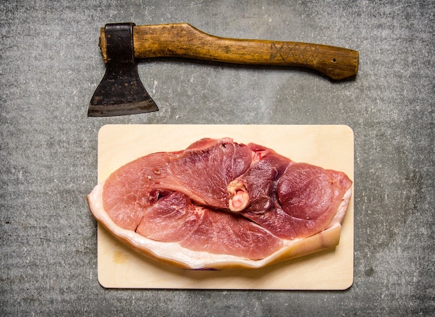 Foto um pedaço de carne de porco crua com uma machadinha para o corte de carne. na mesa de pedra. vista do topo