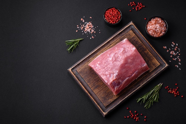 Um pedaço de carne de porco fresca crua em uma tábua de corte de madeira com especiarias e ervas