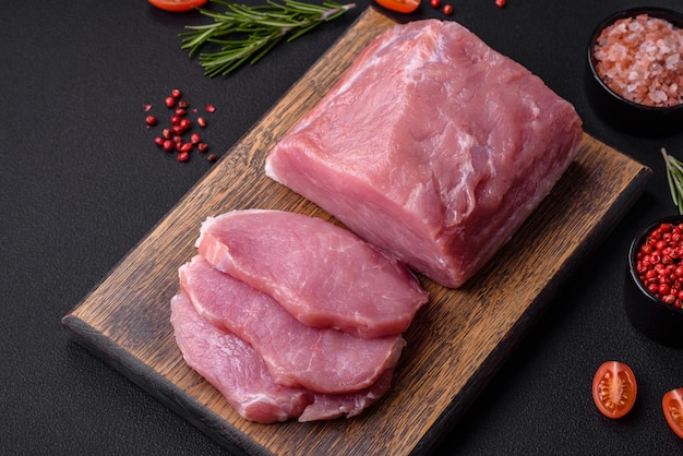 Um pedaço de carne de porco fresca crua em uma tábua de corte de madeira com especiarias e ervas