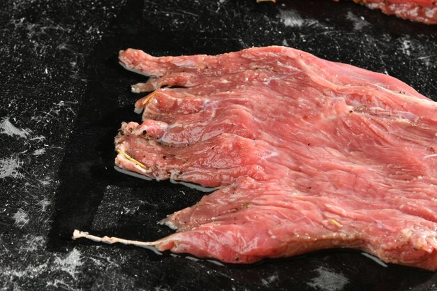 Um pedaço de carne está sobre uma superfície preta com um pedaço de alho.