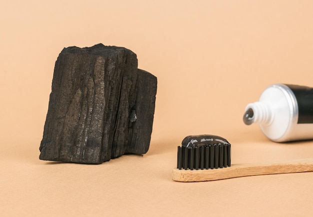 Um pedaço de carvão, uma escova de dentes e pasta de dentes de gel preto sobre fundo bege Clareamento dos dentes e produtos de cuidados dentários