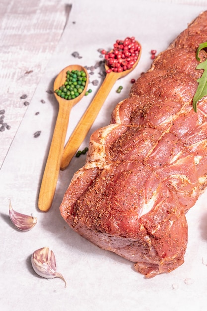 Um pedaço de lombo de porco cru. Carne fresca marinada amarrada com barbante, milho doce e especiarias. Uma luz forte da moda, sombra escura, mesa de madeira velha, close-up