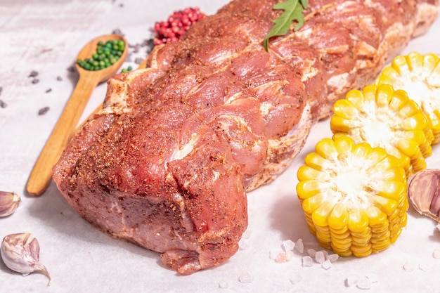 Um pedaço de lombo de porco cru. Carne fresca marinada amarrada com barbante, milho doce e especiarias. Uma luz forte da moda, sombra escura, mesa de madeira velha, close-up