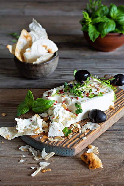 Um pedaço de painel de queijo feta fresco com azeitonas, ervas, especiarias e fatias de pão achatado