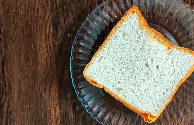 Um pedaço de pão branco colocado em uma placa de vidro com fundo de madeira