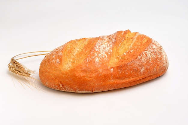 Um pedaço de pão fresco e espigas de trigo ao lado em um fundo branco