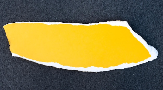 Um pedaço de papel de rascunho de cor amarela com borda rasgada em fundo escuro texturizado