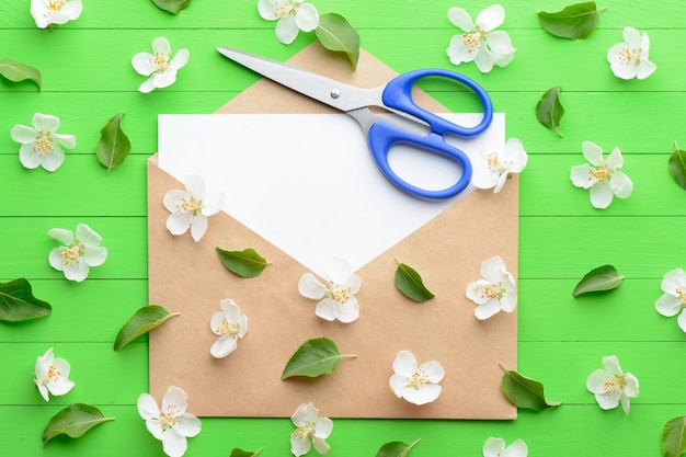 Um pedaço de papel em branco com um envelope sobre fundo verde de madeira