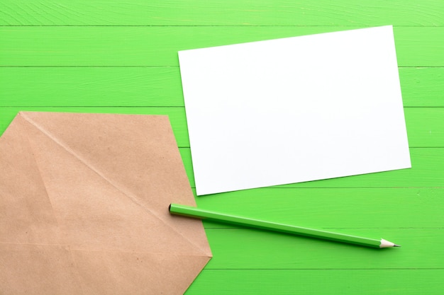 Foto um pedaço de papel em branco com um envelope sobre fundo verde de madeira