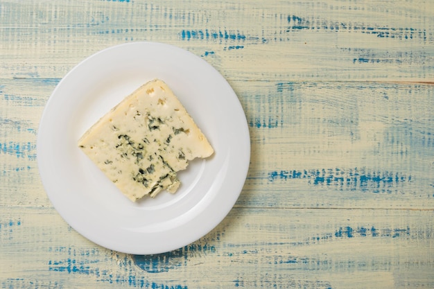 Um pedaço de queijo azul em um prato em um fundo de madeira