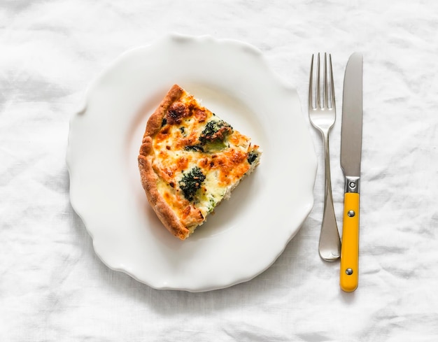 Um pedaço de quiche com espinafre de frango e brócolis e queijo em uma vista superior de fundo claro