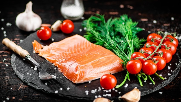 Um pedaço de salmão salgado com tomates e verduras em uma placa de pedra