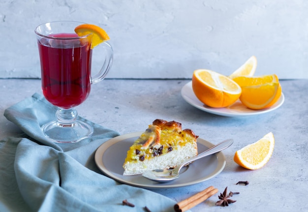 Um pedaço de torta com recheio de laranja, vinho quente, fundo claro, têxteis cinza