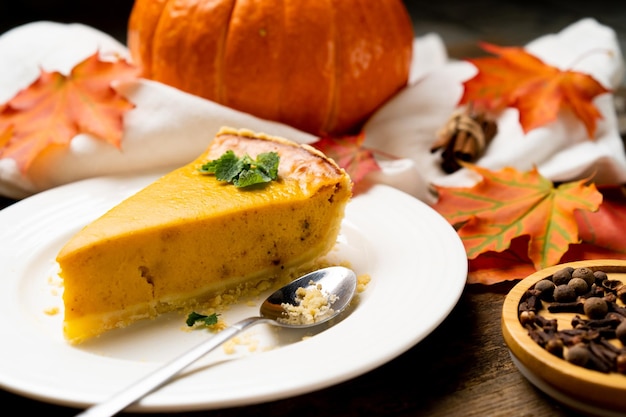 Um pedaço de torta de abóbora americana em um prato branco e uma mesa de madeira