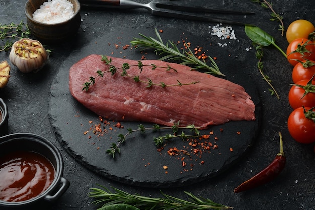 Um pedaço de vitela fresca num prato de ardósia com especiarias e ervas Carne sobre fundo de pedra