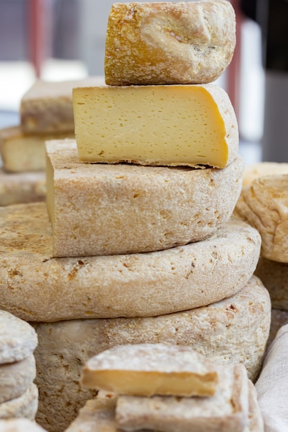um pedaço grande de queijo fica na cabeça do queijo. Cerca de muitos queijos artesanais variados. Vendendo queijo no mercado.