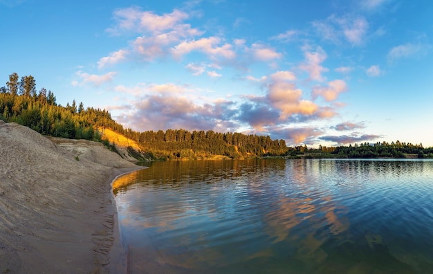 Um penhasco alto na margem de um lago com nuvens coloridas no céu ao pôr do sol