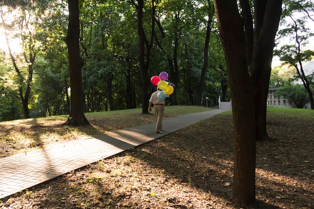 Um pensionista solitário caminha pelo caminho no parque com balões, um idoso está se divertindo no