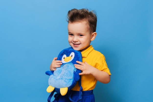 Um pequenino fofo abraça com sua mochila em um fundo azul Garoto engraçado